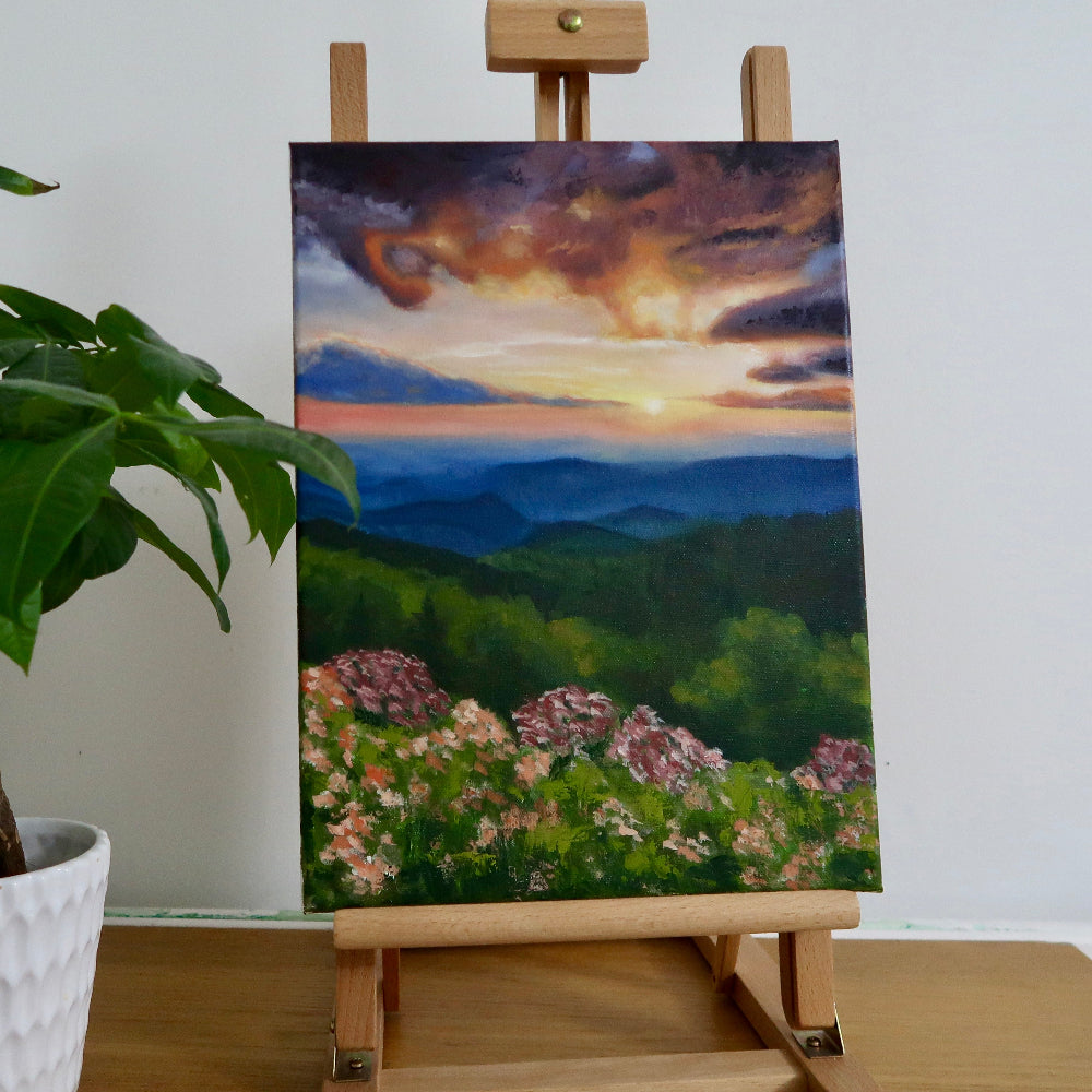 An impressionistic oil painting of a sunset landscape displayed on a wooden easel, with vibrant colors and a focus on the play of light.