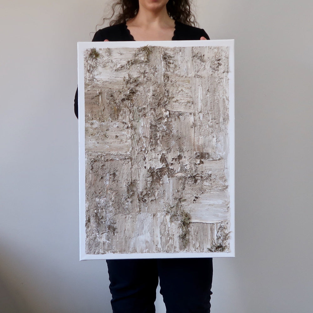 A person holding a abstract acrylic structure painting with predominantly gray and white colors.