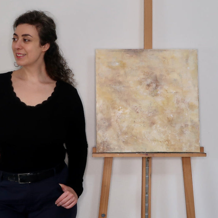 Woman in black outfit standing next to an easel with a painting on a white background