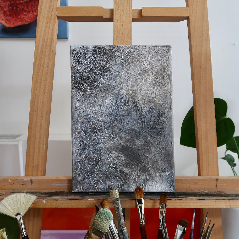 An abstract acrylic landscape painting displayed on a wooden easel with brushes in the foreground.