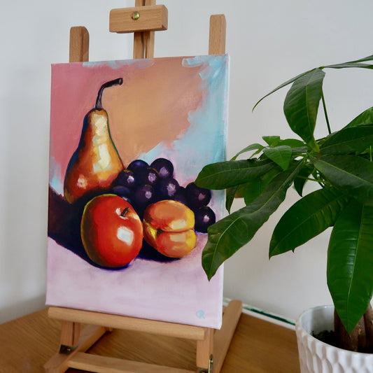 A painting of a colorful fruit still life displayed on a wooden easel, featuring a pear, grapes, and an apple with a pink and yellow background.