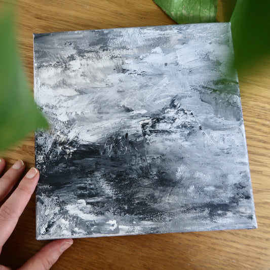 A black and white abstract acrylic landscape painting, depicting a stylized mountain range, held in a person's hand.