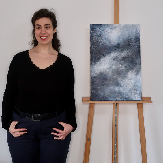 Woman standing next to a painting on an easel against a white wall