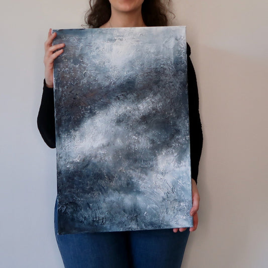 A person holding a abstract acrylic landscape painting with predominantly gray and blue tones.