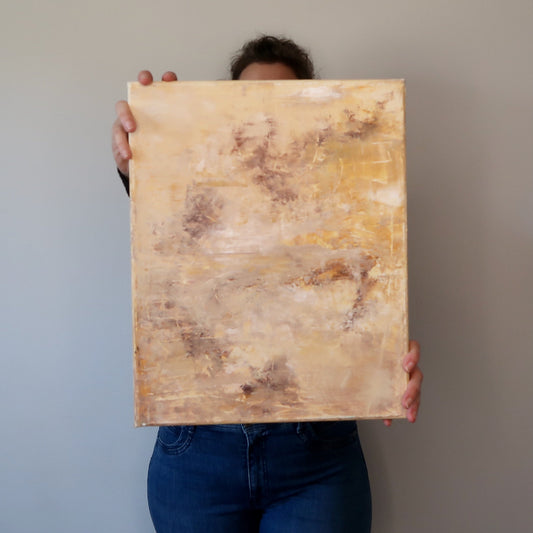 A person holding an abstract acrylic landscape painting with beige and brown tones
