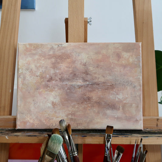 An abstract acrylic landscape painting displayed on an easel with various brushes in the foreground.
